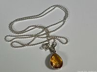 Full view of sterling silver ball chain necklace with attached teardrop shaped faceted citrine pendant.