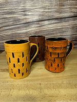 Front view showing all three ceramic cups in the set on a wooden surface with textured patterns and dark brown interiors.