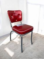 Front angle showing red vinyl padded seat and backrest with silver buttons on backrest, supported by chrome legs and frame.