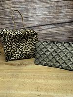 Photo showing both the cheetah print purse and the black embroidered clutch side by side on a wooden surface with rustic wood backdrop.
