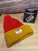 Red and yellow knitted beanie with vintage 49ers patch and black box labeled "Collegiate"