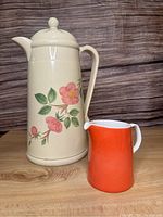 Front view of the Franciscan Desert Rose thermal carafe with orange Sango creamer next to it on a wooden surface