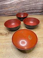 Four lacquer ware bowls set, three open with orange interiors and black exteriors, one with a matching orange lid showing minor wear.