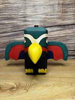 Front view of the colorful vintage wooden carved bird figurine showcasing yellow beak, feet, and painted green, red, blue wings with black and white head.