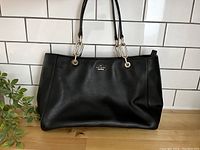 Front view of black leather Kate Spade purse showing logo and gold-tone hardware on straps.