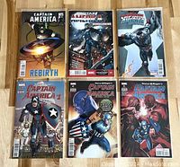 Six Captain America Marvel comics arranged in two rows of three on a wooden surface, showing full covers.