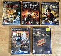 Front view of 5 PlayStation 2 game cases arranged on a wooden surface, showcasing titles and cover art.