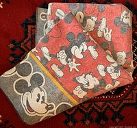 Photo showing full blanket folded, featuring multiple Mickey Mouse prints in different poses on red background with border accents.