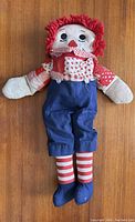 Front view of vintage 19-inch Raggedy Andy doll lying flat, showing full outfit and condition including fabric and yarn hair.