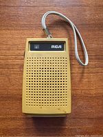 Front view of yellow RCA transistor AM radio with perforated speaker grille and wrist strap on wooden surface.