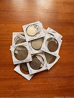 Set of 14 vintage coins in protective paper holders with clear windows, showing varying wear and dates handwritten on the holders.