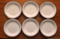 Top-down view of all six small speckled side plates arranged in two rows of three on a wooden surface.