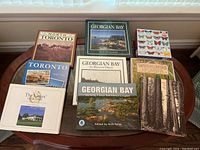 Seven coffee table books and a butterfly puzzle box arranged on a wooden table under a window, showing various covers and titles as seller described.