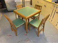 Full view of the Stakmore folding card table with four matching chairs set in a basement room with concrete floor and cupboards along the wall.