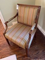 Front angled view of wooden armchair with striped fabric upholstery showing design and condition of chair.
