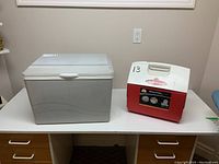 Igloo Playmate Elite cooler in red/white and gray Koolatron cooler side by side on table.