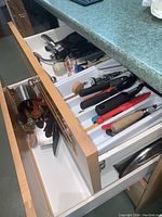 Open kitchen drawers showing assortment of cutlery and kitchen utensils including knives, peelers, ladles, and can openers.