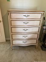Full front view of dresser showing five curved drawers, distressed white finish, gilt trim and hardware.
