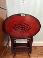 Front view of stacked folded oval tables showing decorative black pattern on reddish-brown wood surface.