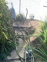 Photo showing garden hose coiled on black metal storage wheel placed on patio with surrounding plants.