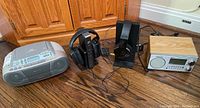 Overall view of all items in lot on wooden floor including Sony CFD-S01 CD radio cassette player, two headphone sets with base stations, and Sangean digital radio receiver.