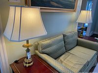 Photo showing one table lamp with fabric rectangular shade and metal base on side table beside couch.