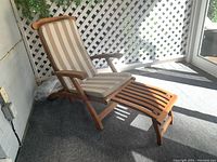Front angle view of the wooden lounger with fold-out stool, showing striped cloth seat pad and armrests.