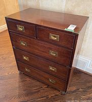 Front angle showing two small top drawers and three larger drawers below with brass recessed handles, chest on wood floor.