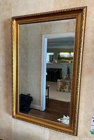 Full view of rectangular mirror hanging on wall showing gold ornate frame and beveled glass edges reflecting room