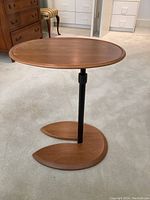 Full view of extendable round wooden side table with black adjustable metal rod and crescent-shaped wooden base.