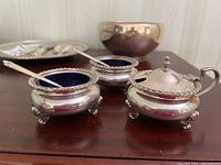 Three condiment bowls and two spoons arranged on table showing overall lot contents