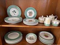 Photo of multiple Wedgwood dishes arranged on shelf including plates and bowls with Sarah's Garden pattern and various serving pieces alongside Covent Garden plates.