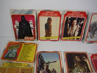 Four vertical trading cards standing upright showing Darth Vader, Chewbacca, Princess Leia, and a checklist card with space paintings near the bottom front.