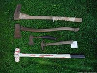 Photo of four axes and one hammer arranged on grass, showing different sizes and styles.