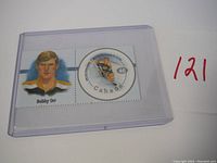 Close-up of 2000 Canada Post Bobby Orr commemorative stamp inside plastic rod-like protective casing, showing portrait and action hockey player image.