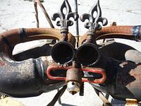 Close-up front view of large rusted metal crab sculpture showcasing round eye tubes, fleur-de-lis metal decorations, and drill chuck mouth detail.