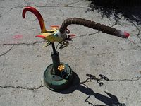 Full side view of the Butt-Sniffer garden sculpture showing the body, wing, long flexible segmented nose, red tail, and green base with valve handles.