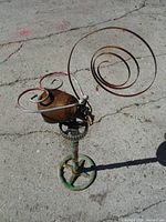 Full view of assembled metal sculpture showing oil can body, coiled wire elements, and valve handle base.