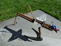 Full view of the garden sculpture showing the rusted metal body and anchor base on a concrete slab with grass background.