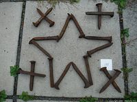 Photo showing 20 old, heavily rusted railroad spikes arranged in the shape of a star and some loose pieces nearby on a concrete surface.