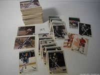 Top view of a large stack of hockey cards alongside several spread-out cards showing player images and identification, with number 107 noted on a paper.