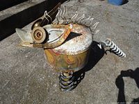 Side and top angled view of the metal chicken sculpture showing rust, gears for eyes, curled wire comb and coiled spring legs.
