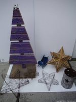 Photo of entire lot shows purple wooden Christmas tree with wire star decorations, two wire stars, blue metal sled, large metal star, and metal candle holder on white background.