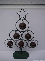 Full view of vintage metal Christmas tree shaped decoration with six rusty jingle bells hanging inside green metal loops, standing on a green scalloped base.