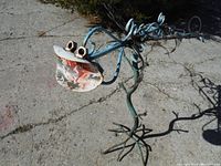 Close view of sculpture's face showing spoon-like mouth and circular eyes made from metal parts.