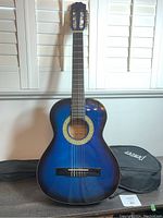 Front view of Denver classical guitar with visible nylon strings, rosette design around sound hole, and accompanying Denver gig bag.