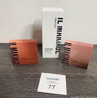Photo of three boxed IL Makiage products on a dark wood surface: two Eye Color Quads in orange and pink packaging, one tall white box for Exfoliating Power Polish.