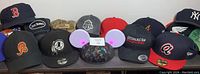 Photo showing a collection of 13 mixed hats and caps including sports team logos and branded caps.