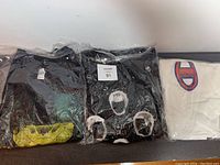 Three black band t-shirts inside plastic packaging displaying parts of the designs and a lot label showing number 91