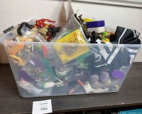Clear plastic storage bin filled with multiple mixed toys and action figures including an Iron Man figure visible on top left corner and various others packed tightly.